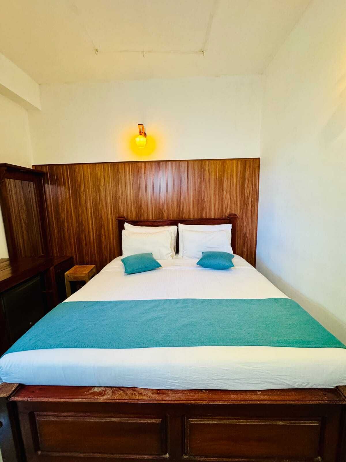 A single bed with a wooden headboard, a blue bedspread, and two pillows.