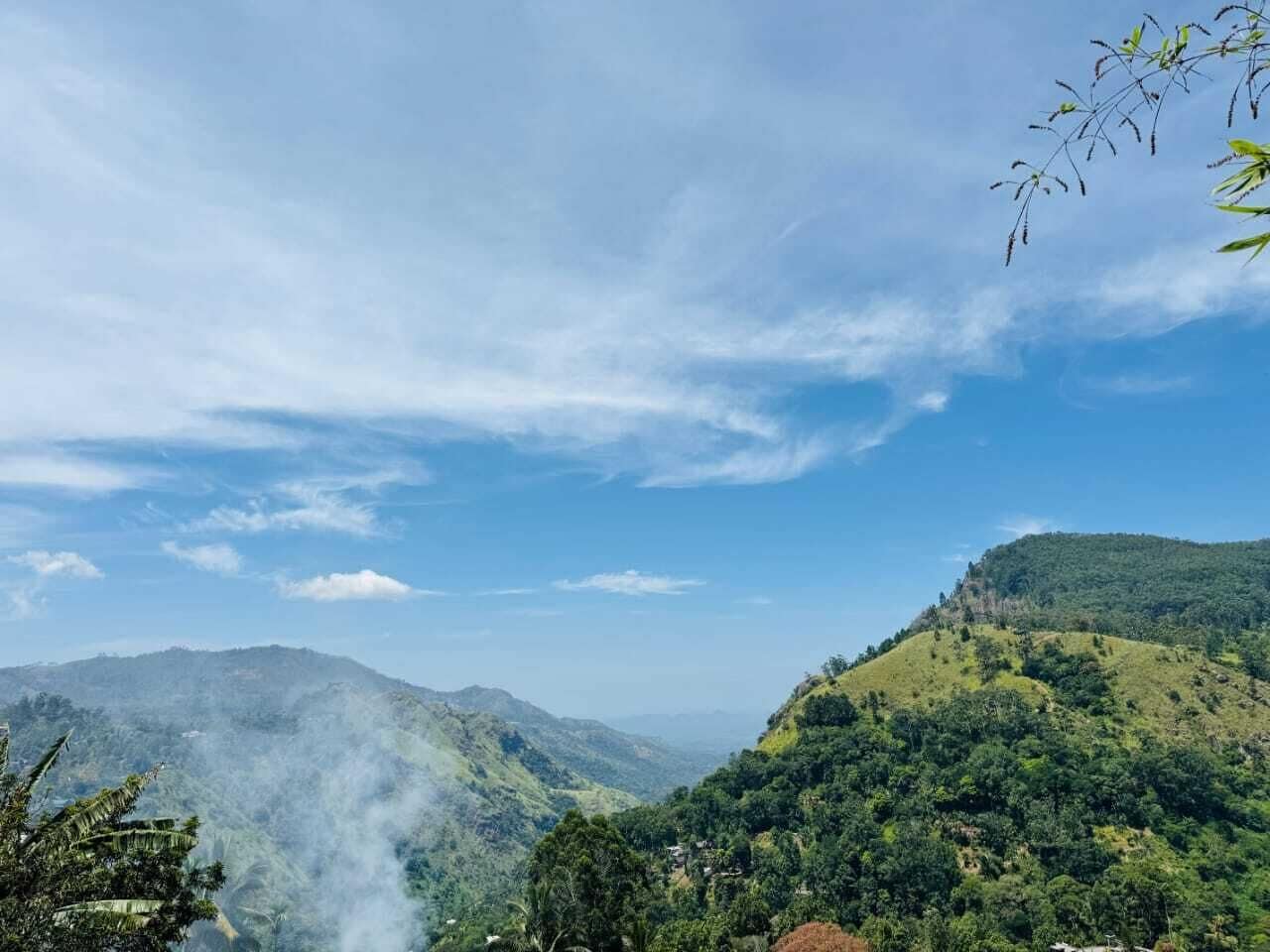 Landskab med bjerge, frodige grønne arealer og en klar himmel.