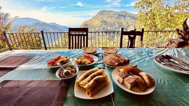 A table set outdoors with various dishes, a view of mountains, and a covered area with chairs. - Nest of peak  (Ella)