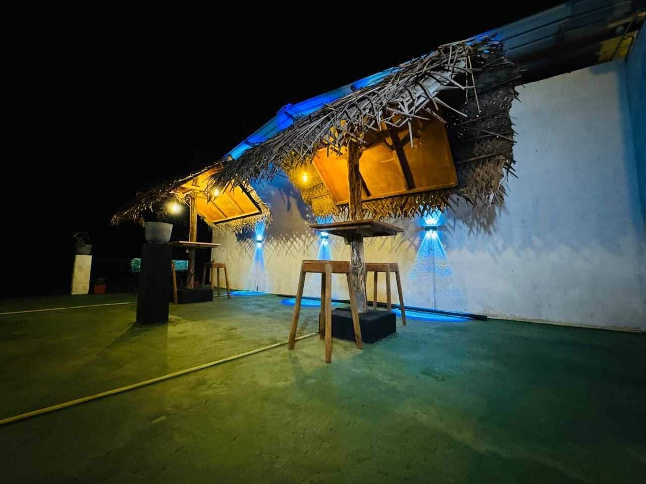 Un edificio con techo de paja, mobiliario de madera e iluminación ambiental azul.