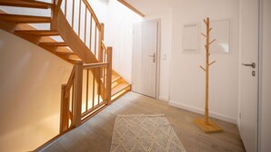 Eine Holztretreppe führt zu einem Raum mit Kleiderhaken und einer Tür mit Lichtschalter.