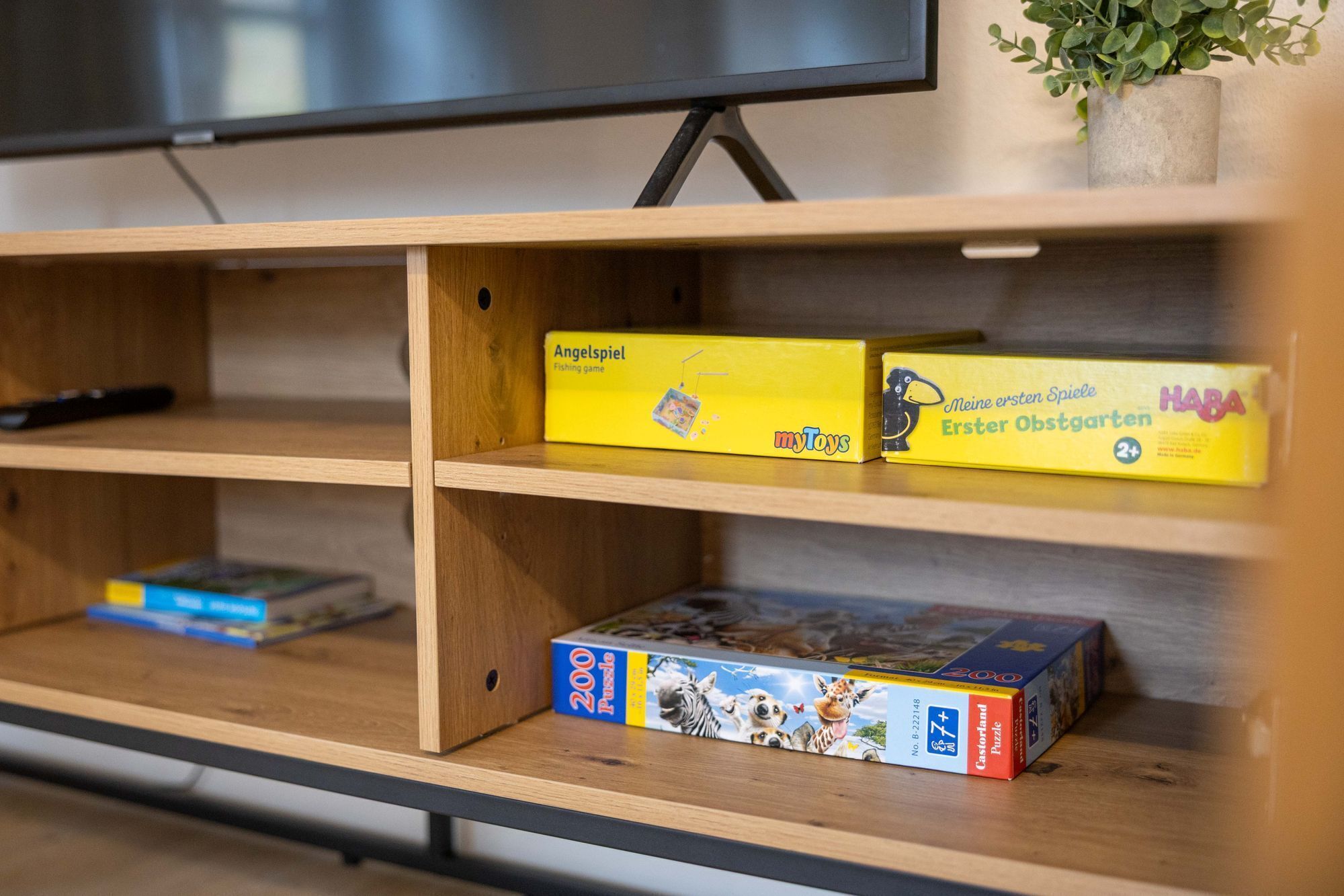 Une étagère en bois sur laquelle sont posés divers jeux de société, et une télévision au-dessus.