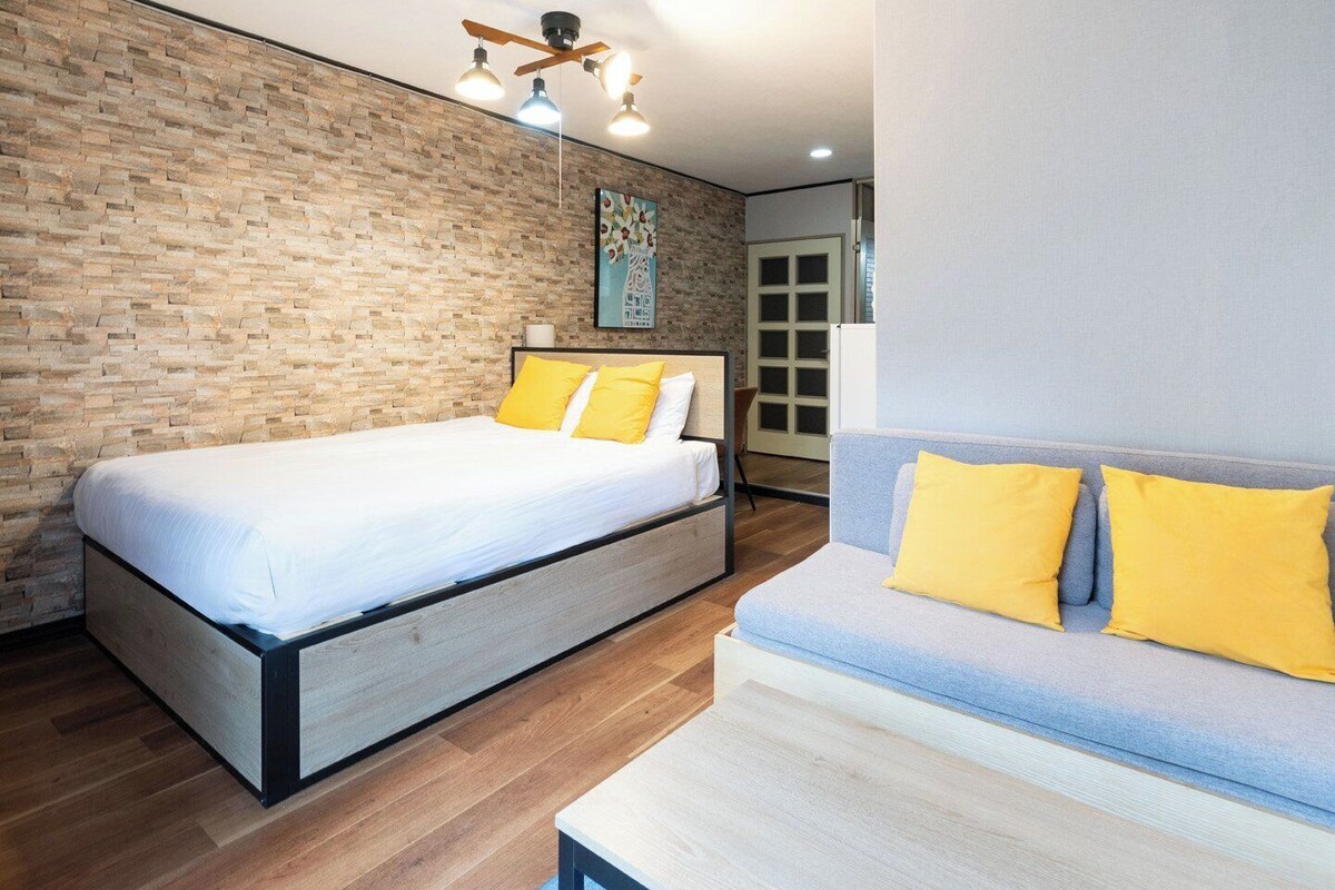 A room with a bed, a sofa, a brick wall, a ceiling fan, and a door.