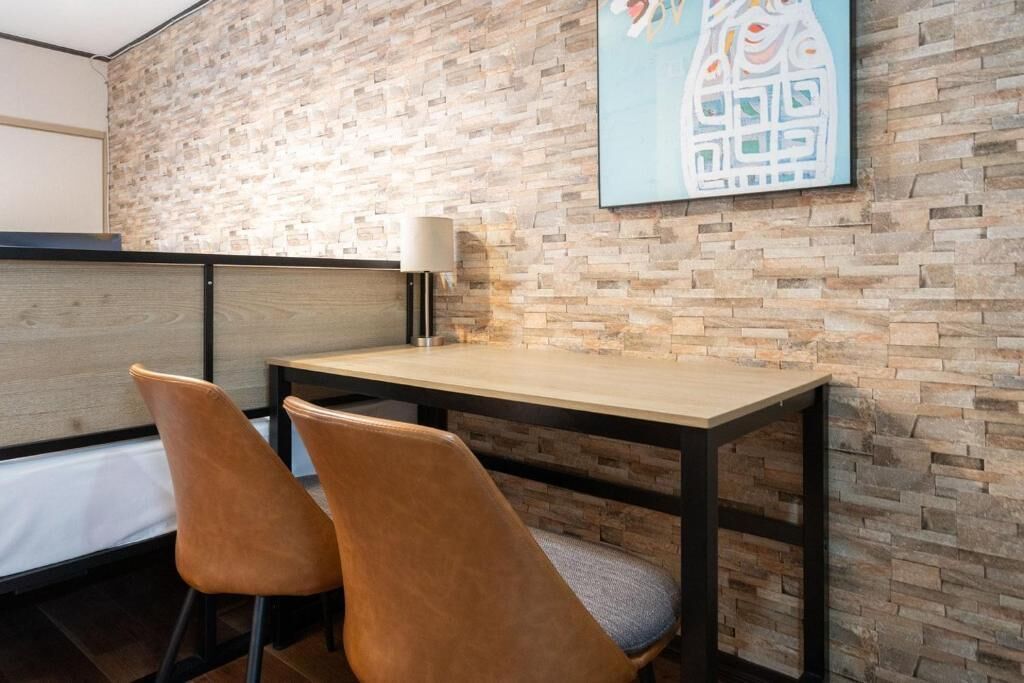 Ein Essbereich mit Holztisch und zwei Stühlen, einer Wand mit Ziegelmuster und einem Gemälde über dem Tisch.