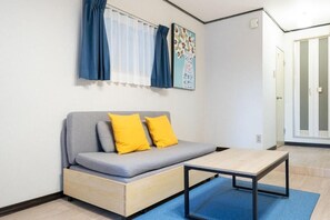 Ein modernes Zimmer mit einer Couch, einem kleinen Tisch, einem Fenster mit Vorhängen und einer Tür.
