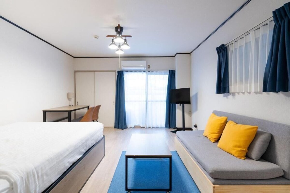 A hotel room with a bed, a sofa, a desk, and a ceiling fan.