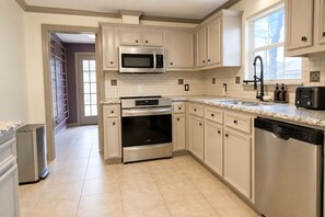 A kitchen with white cabinetry, a stainless steel microwave, oven, and dishwasher, a tiled backsplash, and a window providing natural light. - Central Location - Heights & Downtown 5 Mins - 3BR - Groups, Family, Yard, Pets (Houston)