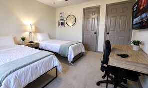 A hotel room with two beds, a desk with a chair, a TV mounted on the wall, and a door. - Central Location - Heights & Downtown 5 Mins - 3BR - Groups, Family, Yard, Pets (Houston)