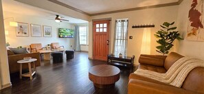 A living room with a brown leather sofa, a round coffee table, and a TV on the wall. - Central Location - Heights & Downtown 5 Mins - 3BR - Groups, Family, Yard, Pets (Houston)