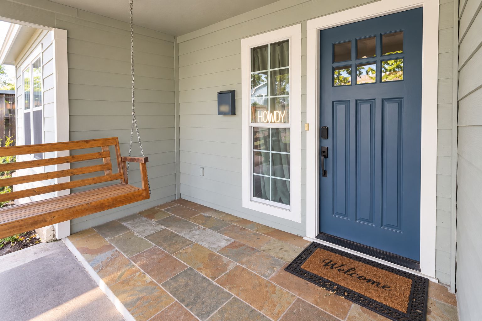 A front porch with a swing, a blue door, and a welcome mat.