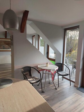 Un espace repas comprenant une table et des chaises, un luminaire suspendu et un escalier menant à un balcon avec des sièges d’extérieur.