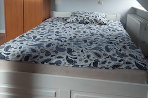 A bed with a patterned bedspread and pillow, a wooden wardrobe, and a white headboard. - Apartment in Sopot Near Monte Cassino Street (Sopot)