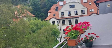 A balcony with a railing overlooking a garden and a building with a red-tiled roof.