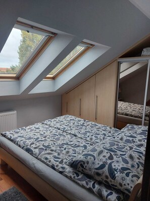 Une chambre avec un puits de lumière, un lit avec une literie à motifs, des armoires en bois et une armoire avec des portes miroir.