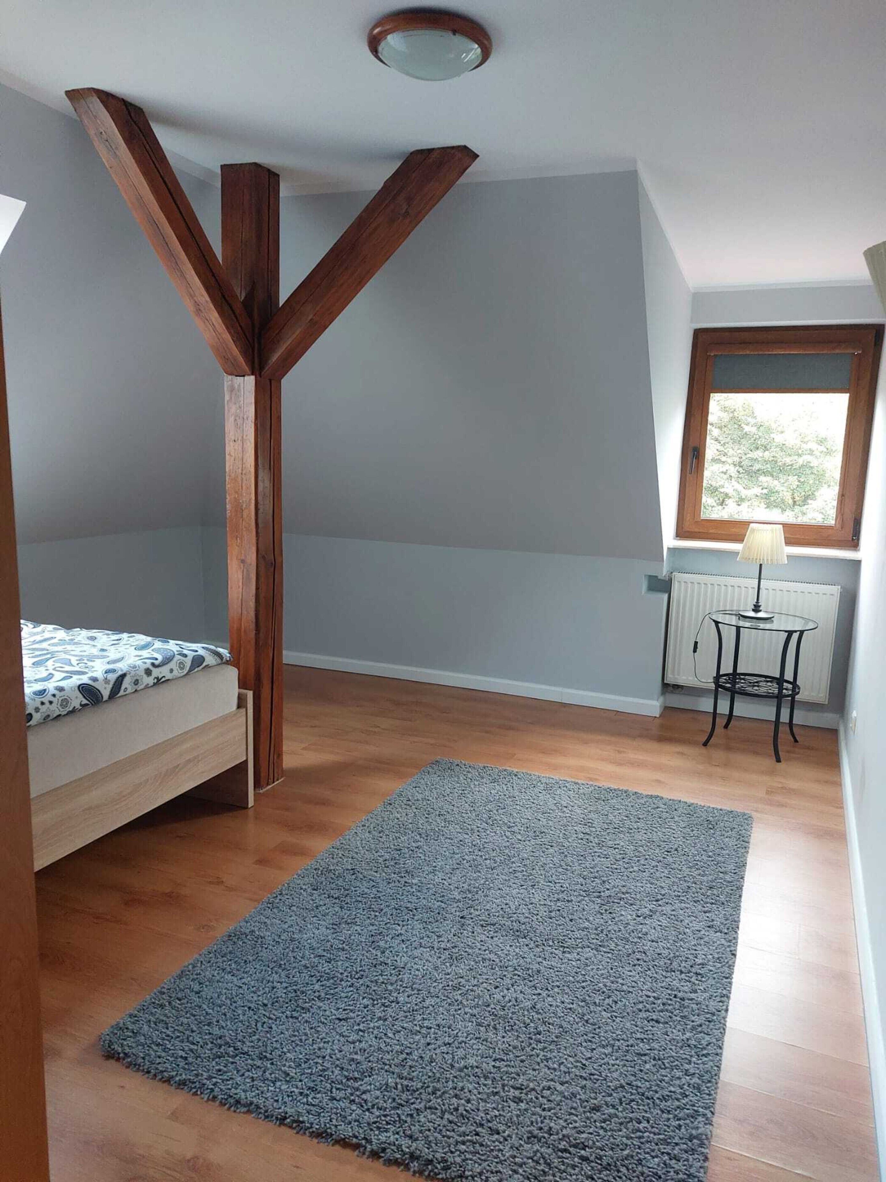 Une pièce avec un plafond en pente, un lit, une petite table avec une lampe et une fenêtre.