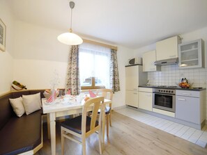 A compact kitchen with a dining area, wooden furniture, and a window with curtains. - Apartment in Flachau With Mountain Views (Flachau)