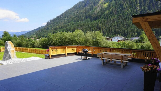Eine Terrasse mit Holzdeck, einem Grill und einer Holzbank.
