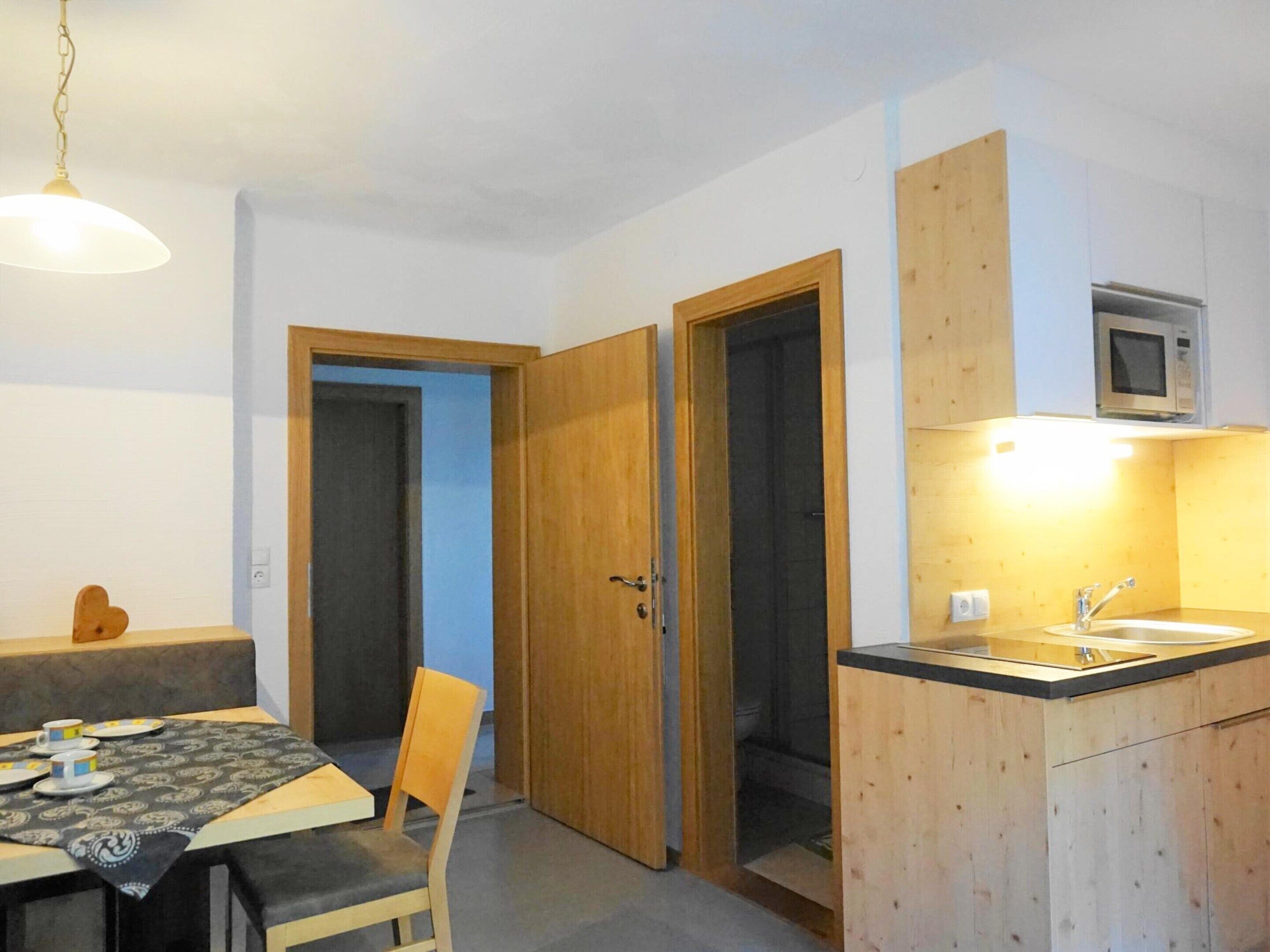 A compact kitchen with a microwave, a sink, and a dining area with a table and chairs.