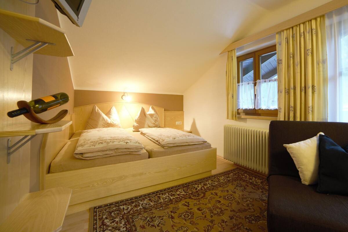 Une chambre à coucher comprenant un lit, une table de chevet, un téléviseur fixé au mur, une fenêtre avec des rideaux et un radiateur.