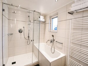 A modern bathroom with a glass-enclosed shower, a standalone bathtub, and a window providing natural light. - Tranquil Apartment in the Centre of Seefeld (Seefeld in Tirol)