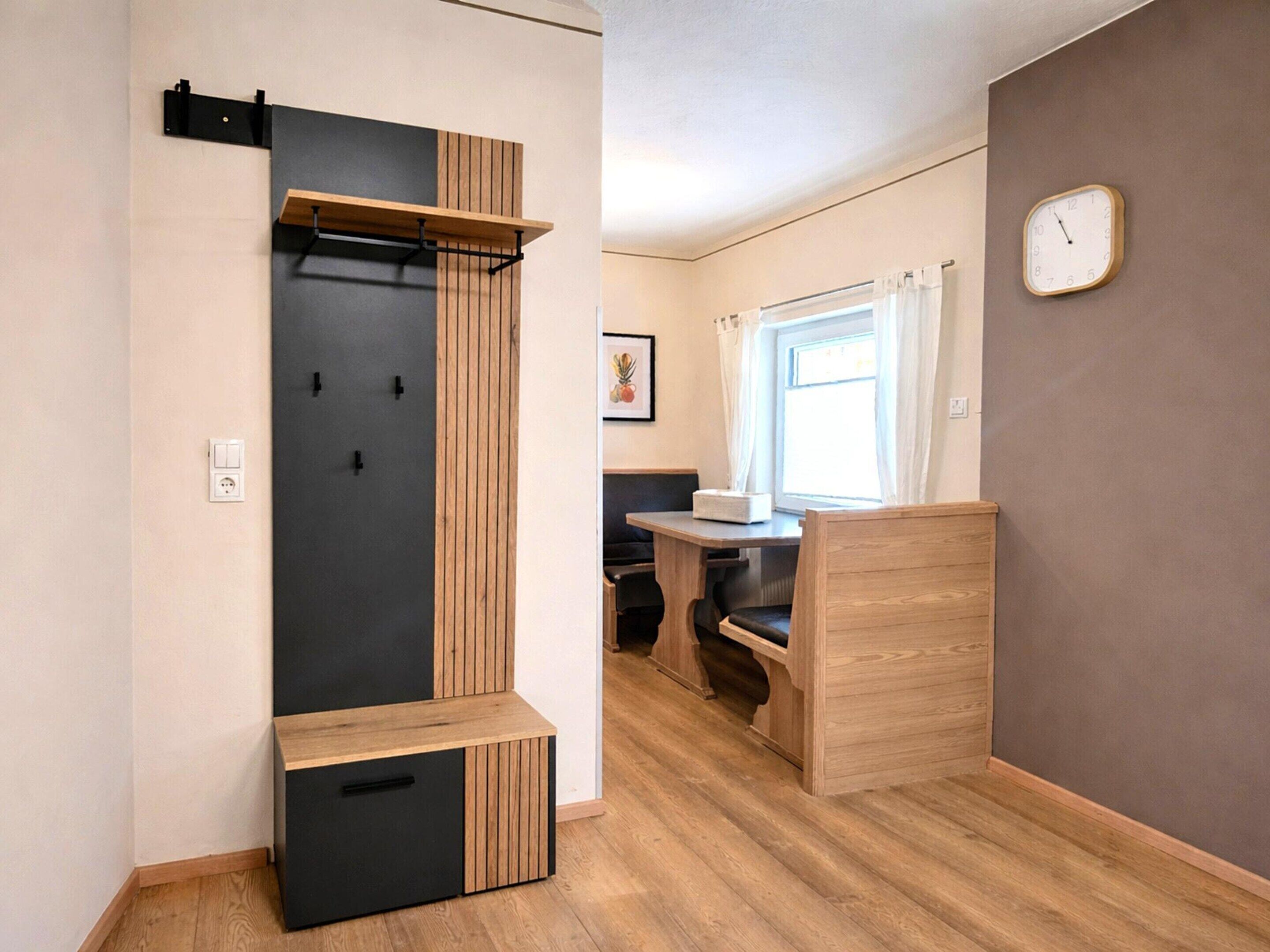 Une petite pièce comprenant un lit, une petite table, une fenêtre avec des rideaux, une horloge et une étagère fixée au mur.