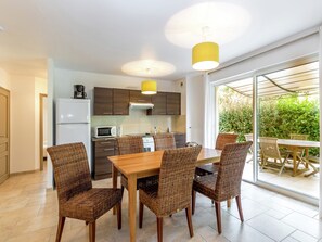 A modern kitchen with dark cabinets, a white refrigerator, a microwave, and a stove. There is a dining area with a wooden table and wicker chairs. - Apartment in Montauroux With Pool & Forest Views (Montauroux)