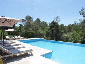 Una piscina con sillas de descanso y una sombrilla, rodeada de árboles.