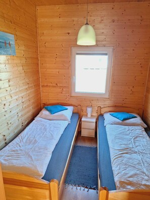 Une petite cabane avec deux lits en bois, une fenêtre et un luminaire suspendu.