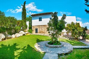 A white building with stone walls, a stone pathway, and a circular stone planter with a tree. - Finca in Muro With Panoramic Views (Santa Margalida)
