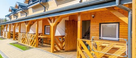 A row of wooden cabins with balconies, a paved walkway, and a covered outdoor area.