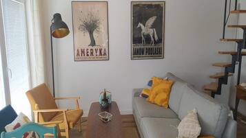 Una sala de estar con un sofá, una silla, una mesa de centro y dos carteles colgados en la pared.
