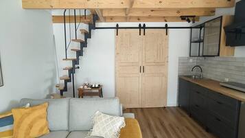 Un espacio habitable compacto con escaleras, un sofá, una zona de cocina y suelo de madera.