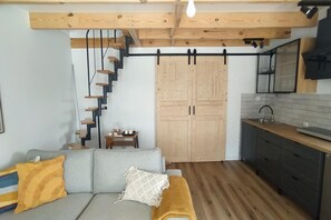 A compact living space with a staircase, a sofa, a kitchen area, and wooden flooring. - Holiday Home, Sauna, Jacuzzi, air Conditioning (gmina Sianów)