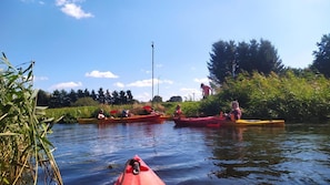 A calm river with kayaks, a clear sky, and greenery along the banks.