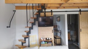 A room with a wooden staircase, a flat-screen TV mounted on the wall, and a small table with items on it.