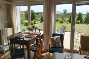 A dining area with a table set for four, chairs, and a view of a garden through large sliding glass doors. - Holiday Home, Sauna, Jacuzzi, air Conditioning (gmina Sianów)