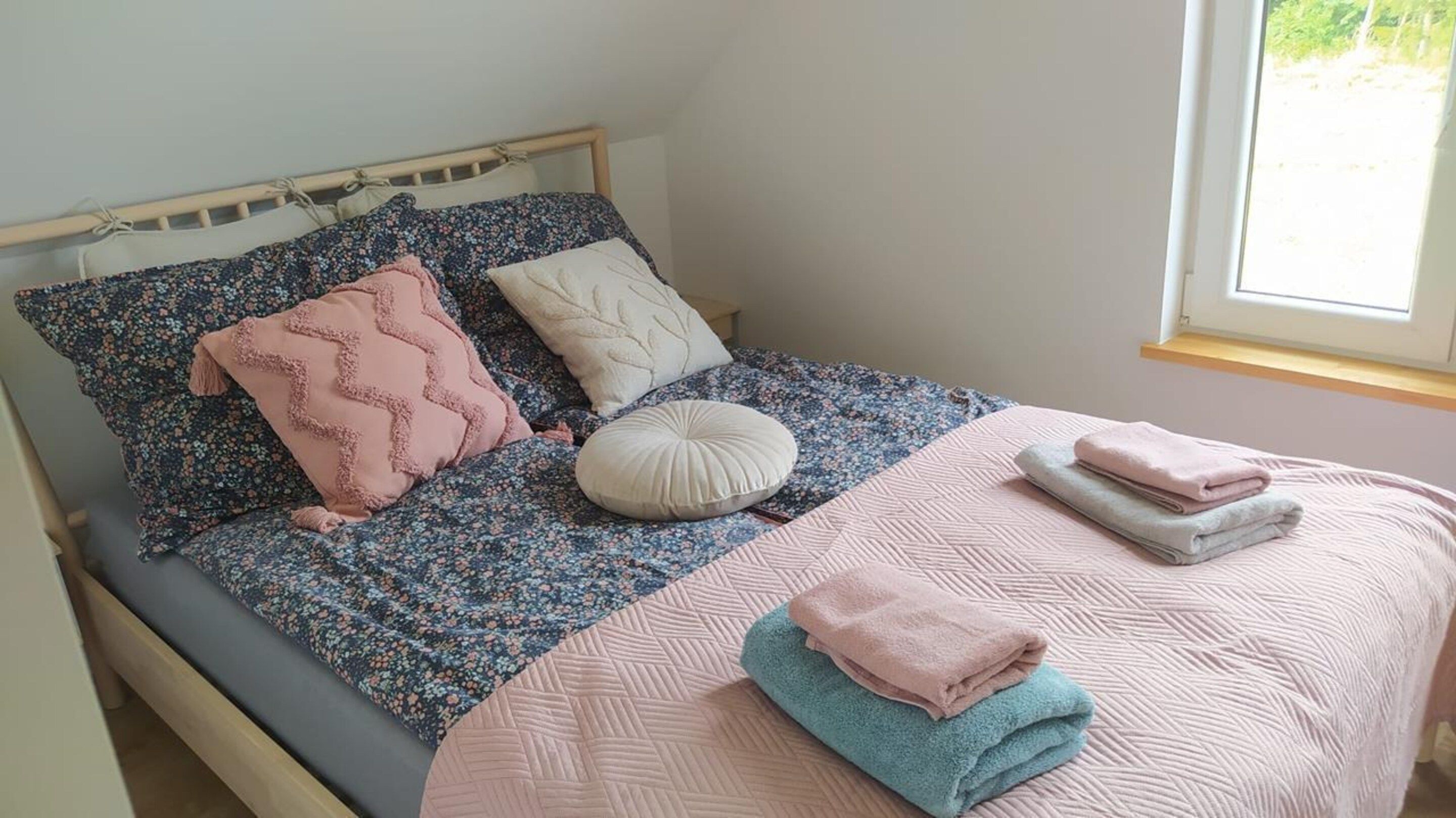 A bed with floral bedding, a wooden headboard, and a window with a view of greenery.