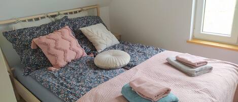A bed with floral bedding, a wooden headboard, and a window with a view of greenery.