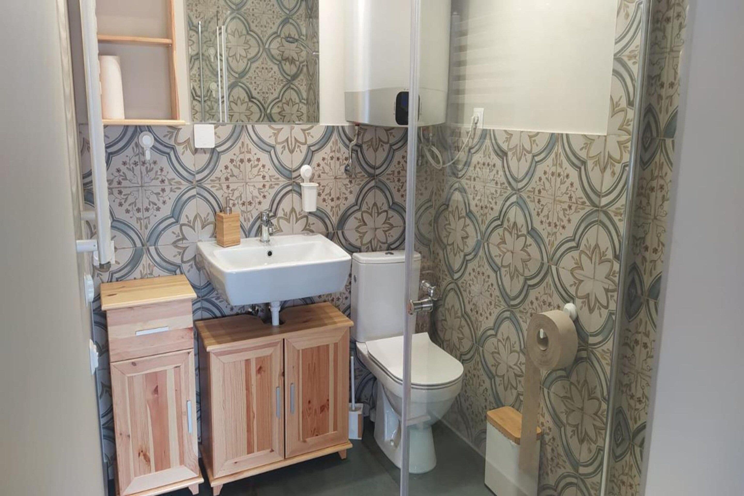 A bathroom with a wooden cabinet, a white sink, a toilet, and patterned wallpaper.