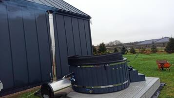 Un edificio metálico grande con una chimenea, un jacuzzi y un calentador de agua en una terraza de madera.