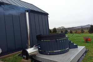 A large metal building with a chimney, a hot tub, and a water heater on a wooden deck. - Holiday Home, Sauna, Jacuzzi, air Conditioning (gmina Sianów)