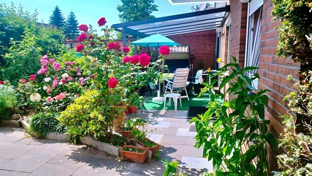 Eine Terrasse mit Kübelpflanzen, einem Tisch, Stühlen und einem blauen Sonnenschirm.