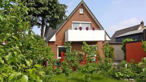 Ein Wohngebäude mit roter Backsteinfassade, einem weißen Balkon und einem Garten mit verschiedenen Pflanzen.