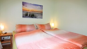 Ein ordentlich bezogenes Bett mit rosa Bettwäsche, zwei Nachttische mit Lampen und ein Bild mit Strandmotiv an der Wand.