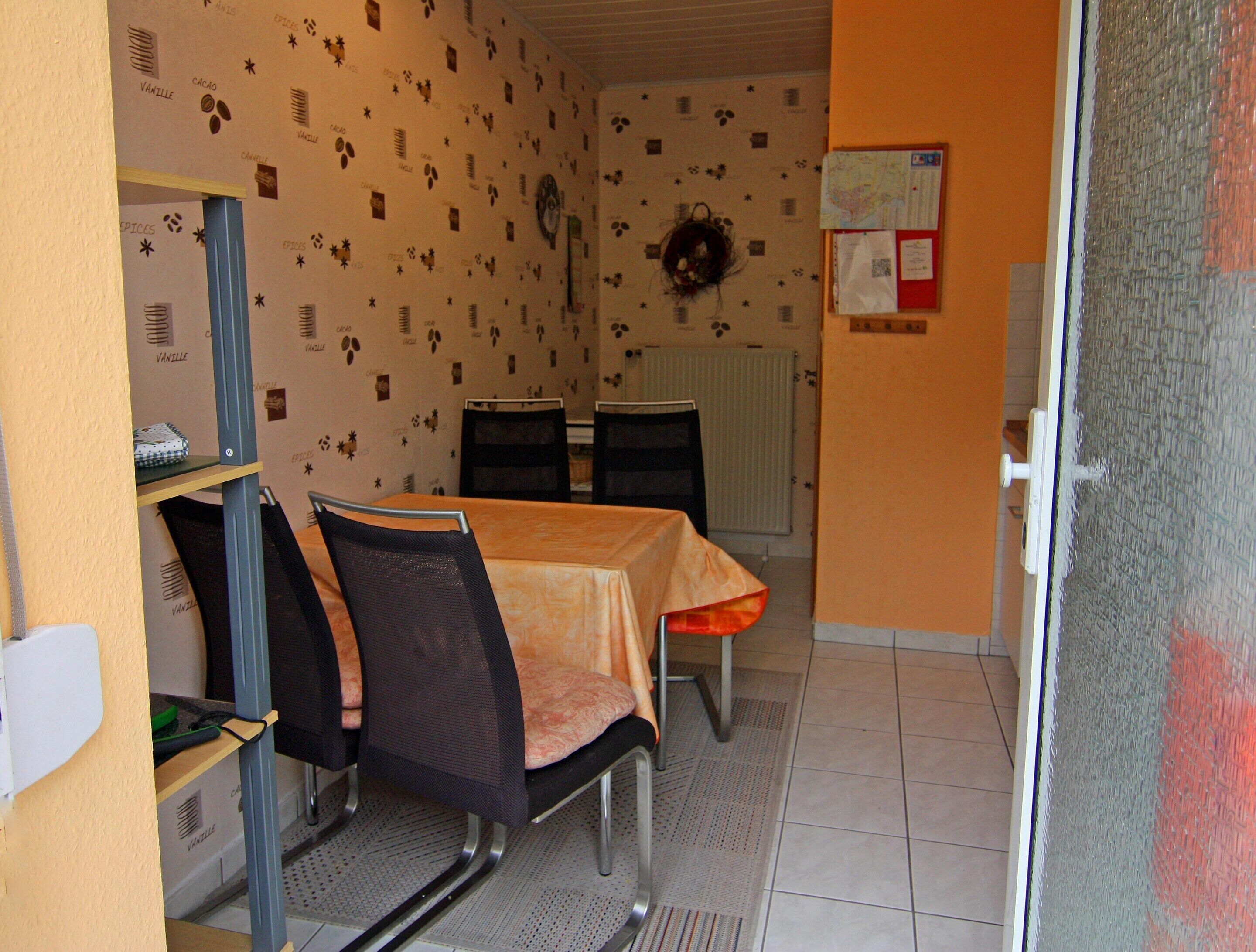 A dining area with a table, chairs, a wall clock, a bulletin board, and a radiator.