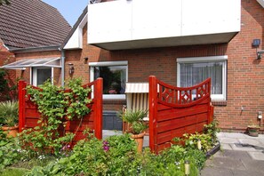 A residential building with a brick facade, a red gate, and a garden with various plants. - Wohnung in Busum mit Garten (Büsum)