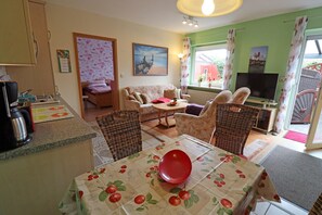 A living room with a sofa, chairs, a television, and a dining table with a red bowl. - Wohnung in Busum mit Garten (Büsum)