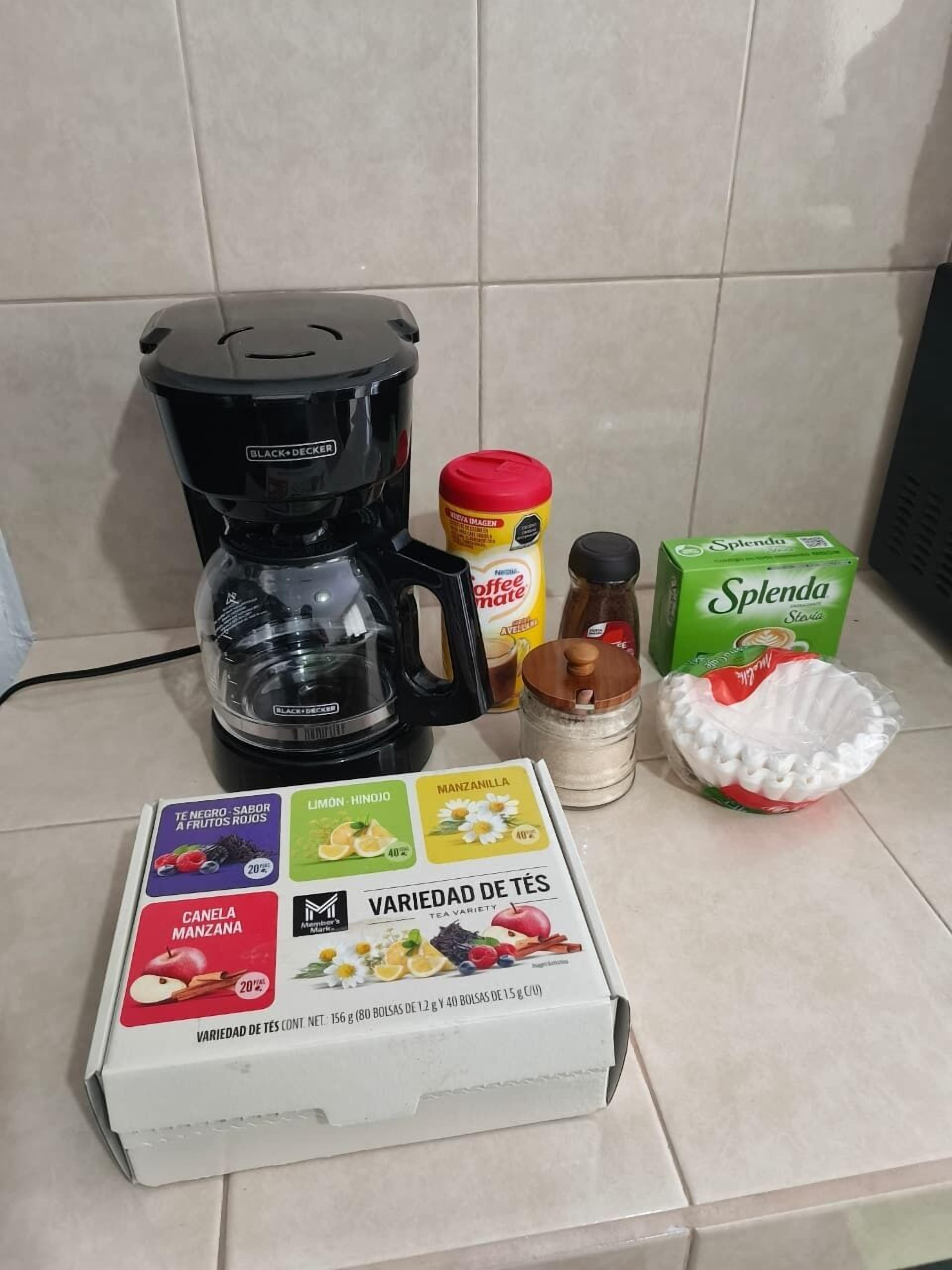 Un comptoir de cuisine avec une machine à café, une boîte d’édulcorant Splenda, un pot de crème à café, un récipient à épices et une boîte contenant différents types de thé.