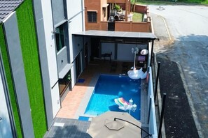 Ein Schwimmbecken mit Liegebereich, einer überdachten Terrasse und Blick auf die Straße.