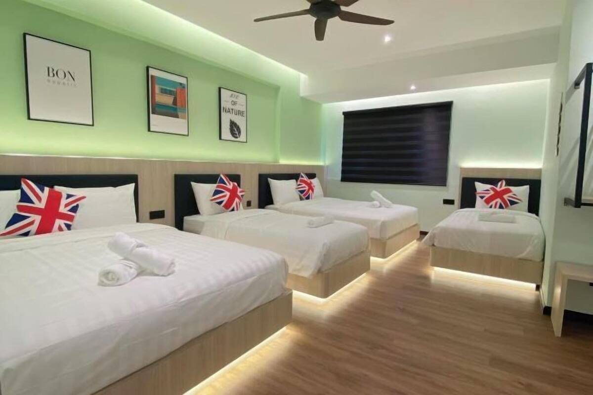 Une chambre d’hôtel avec trois lits, chacun agrémenté d’un coussin orné du drapeau britannique, un ventilateur de plafond et des œuvres d’art encadrées accrochées aux murs.